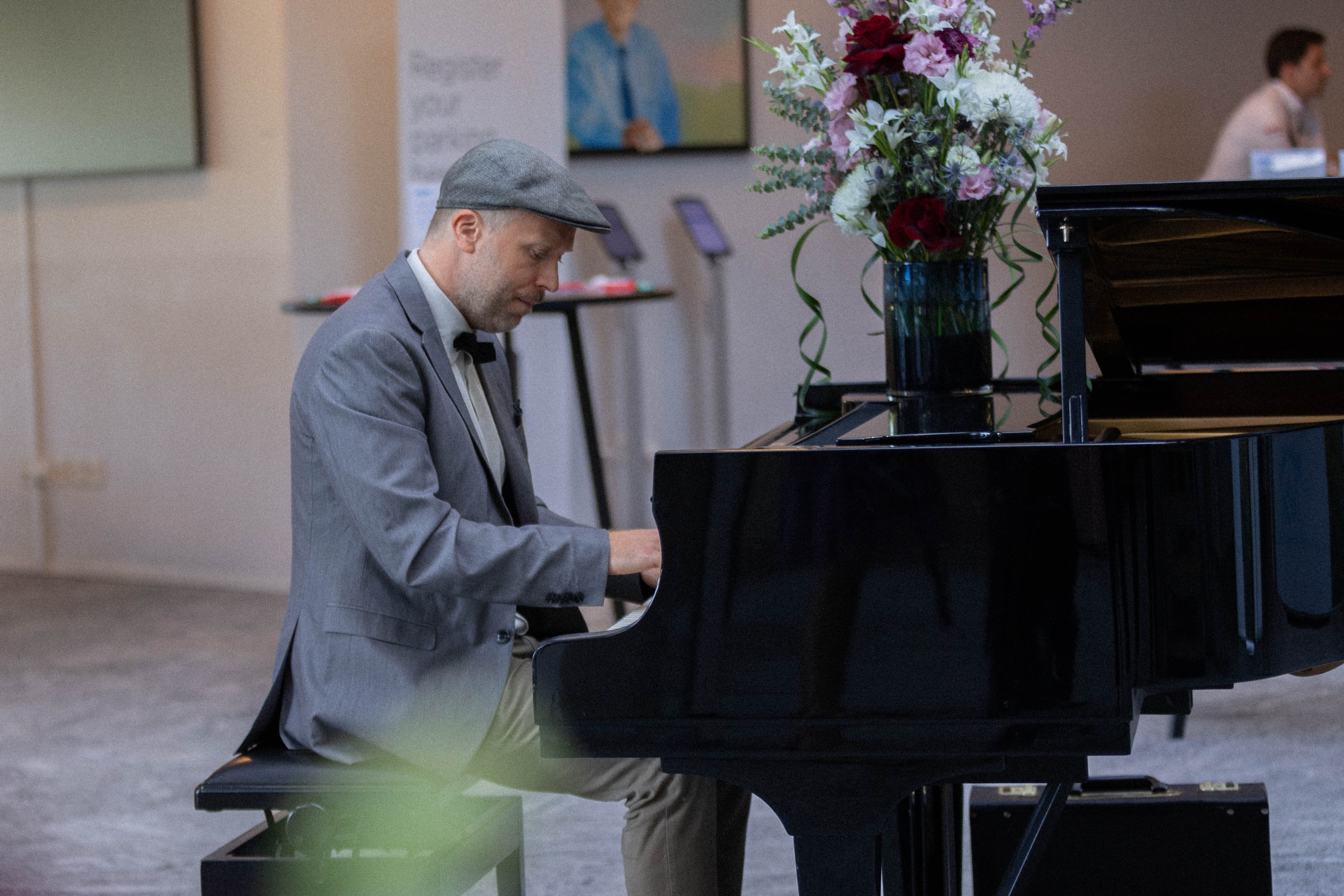 Pianist i grå jakke ved flygel under firmaarrangement — baggrundsmusik til julefrokost eller firmafest