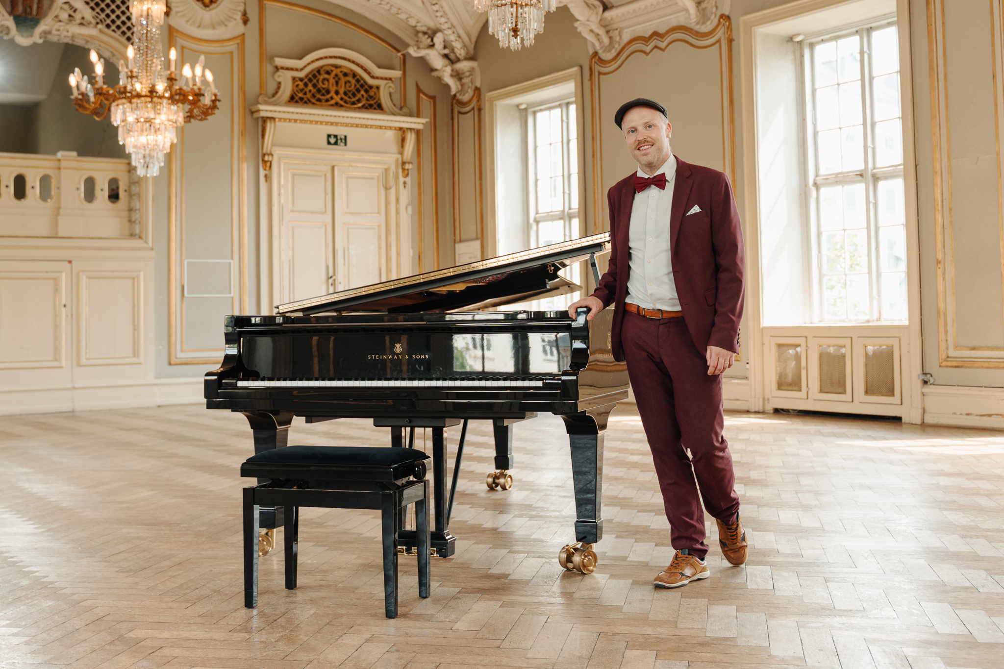 Oscar Gilbert stående ved Steinway-flygel med smil — klar til reception
